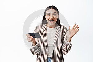 Excited brunette girl winning on mobile phone video game, holding smartphone horizontally, scream from joy and smiling