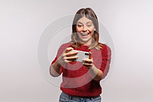 Excited brunette woman holding mobile phone horizontal and smiling joyfully, watching funny vid online, reading joke photo