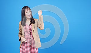 Excited business asian woman holding fist arms hand smile happiness success job or lucky standing over isolated blue background.