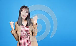 Excited business asian woman holding fist arms hand smile happiness success job or lucky standing over isolated blue background.