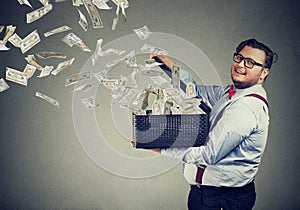 Excited business man opening a box letting dollar banknotes to fly away