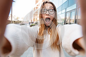 Excited business woman posing walking outdoors near business center wearing eyeglasses take selfie by camera