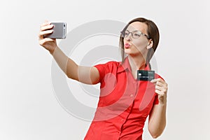 Excited business woman in red shirt doing taking selfie shot on mobile phone with credit bank card, cashless money