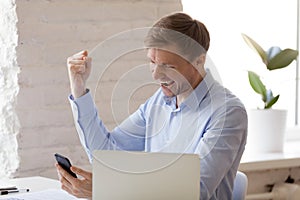 Excited businessman celebrating business achievement, using phon