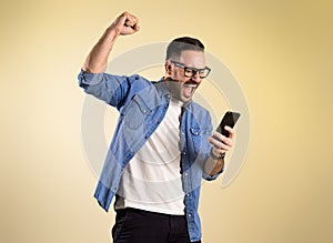 Excited businessman dressed in denim shirt screaming and raising hand while reading good news over mobile phone. Young man