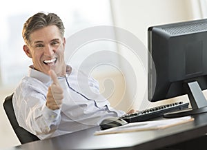 Excited Businessman Gesturing Thumbs Up At Desk