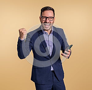 Excited businessman in suit laughing and shaking fist after reading good news on smartphone