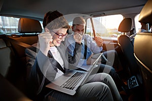 Excited businesspeople looking at laptop in car on trip