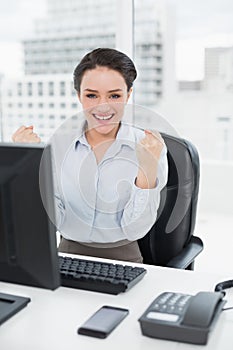 Excited businesswoman clenching fists at office desk