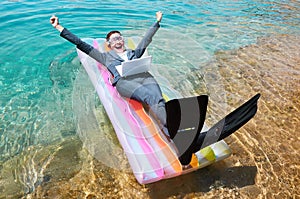 Excited businesswoman floating on lilo with laptop