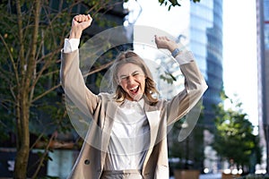 Excited businesswoman screams and celebrates, lifts hands up, does hooray gesture, celebrates victory, achieve goal