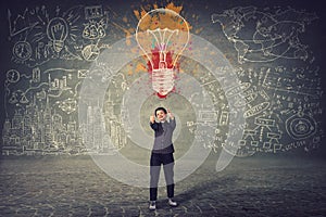 Excited businesswoman, showing thumbs up gesture, stands in front of a wall with drawn colorful light bulb and business sketches.