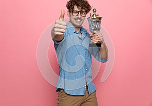 Excited casual guy holding trophy and making thumbs up sign