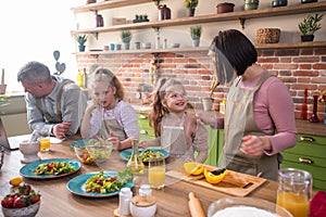 Excited Caucasian family parents and two kids girls happy playing rock paper scissors before start to cook the dinner