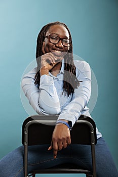 Excited cheerful african american pretty attractive woman sitting on chair while smiling at camera