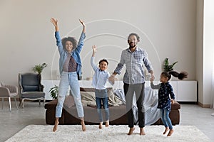 Excited cheerful African parents and little kids jumping on carpet