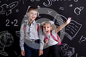 Excited and cheerful schoolkids standing before the chalkboard as a background with a backpack on their backs showing