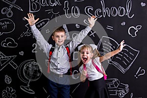 Excited and cheerful schoolkids standing before the chalkboard as a background with a backpack on their backs showing