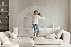 Excited cheerful small 7s kid girl jumping on sofa.