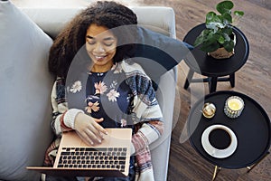 Excited cheerful young black woman using laptop computer on sofa at home