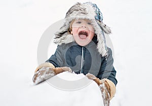 Excited child playing with a snow. Cute child in winter hat having fun with snowball in winter park. Winter clothes for