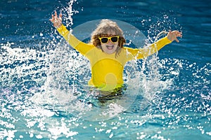 Excited child splashing water in pool. Little kid splashing in blue water of swimming pool. Cute boy swimming and