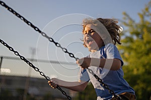 Excited child swinging on chain swing on city kids playground. Swing ride. Cute child having fun on a swing on summer