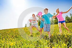 Excited children with balloons run in green field