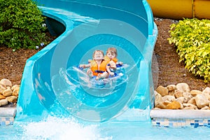 Excited children in water park riding on slide with float