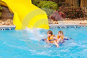 Excited children in water park riding on slide with float