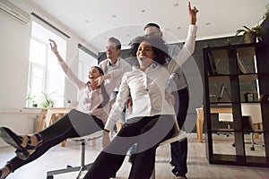 Excited colleagues having fun riding chairs during work break