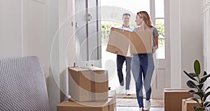 Excited Couple Carrying Boxes Through Front Door Of New Home On Moving Day