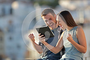 Excited couple checking tablet online content in a town