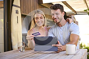 Excited Couple With Credit Card Using Digital Tablet At Home To Book Holiday Or Shop Online