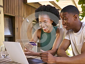 Excited Couple With Credit Card Using Laptop At Home To Book Holiday Or Shop Online
