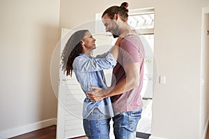 Excited Couple Hugging By Open Front Door In Lounge Of New Home