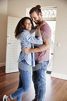 Excited Couple Hugging By Open Front Door In Lounge Of New Home