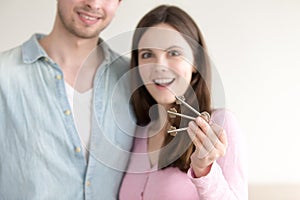 Excited couple showing new keys in focus, real estate purchase