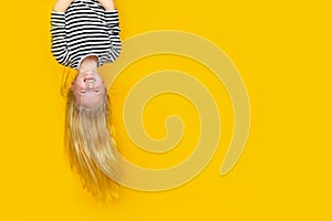 Excited crazy little blonde girl hanging happy upside down over isolated yellow studio background. Emotion, expression