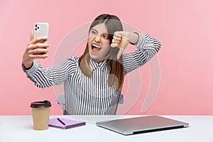 Excited crazy woman blogger in striped shirt showing thumbs down dislike gesture looking at smartphone camera, criticizing and