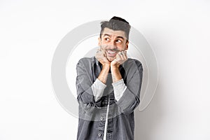 Excited cute young man look dreamy at upper left corner, waiting for parcel, daydreaming or imaging something, standing