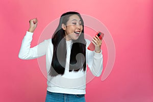 Excited delighted asian girl hold phone feeling euphoric from mobile online game win celebrating good news