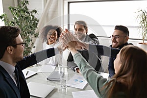 Excited diverse colleagues give high five at meeting