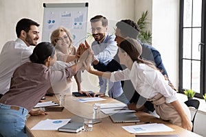 Excited diverse employees give high five at meeting