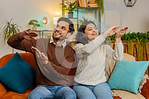 Excited diverse rich young couple wasting or throwing money hand gesture sitting on sofa at home