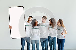 Excited diverse volunteering people showing white empty smartphone screen