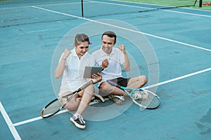 excited doubles tennis players sitting looking at digital tablet together