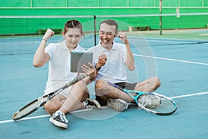 excited doubles tennis players sitting looking at pad screen together