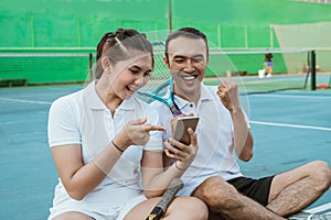 excited doubles tennis players using cell phones together while sitting