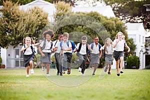 Excited Elementary School Pupils Wearing Uniform Running Across Field At Break Time photo